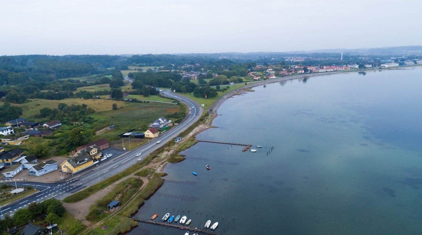 Luftfoto: kroen ved vejen langs fjorden, med Aabenraa by i baggrunden