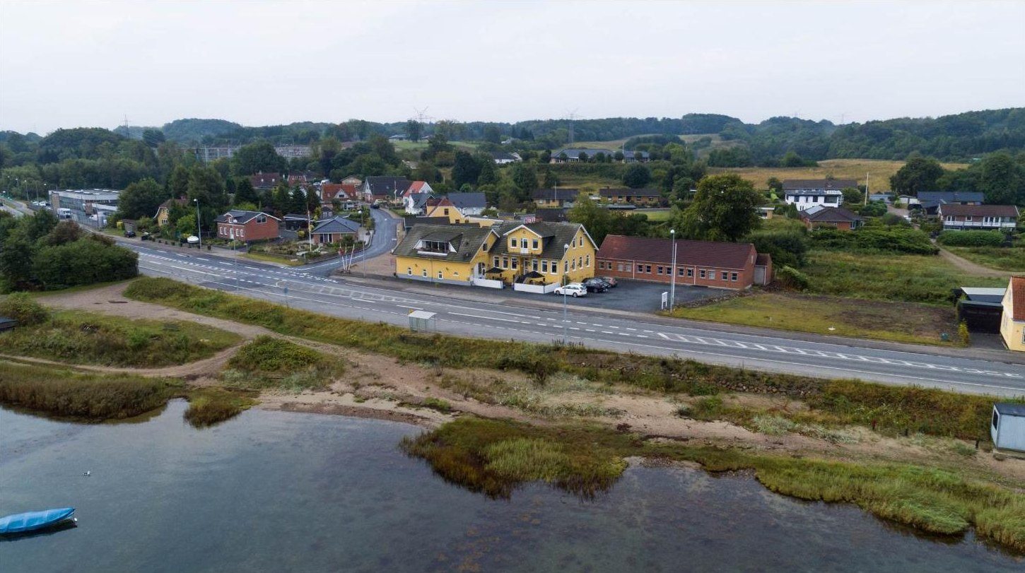 Luftfoto: den gule kro ved hovedvejen, set fra fjorden