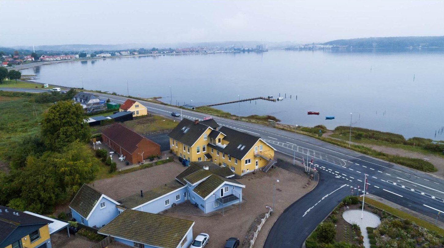 Luftfoto af den gule kro ved vejen langs Aabenraa Fjord med byen i baggrunden